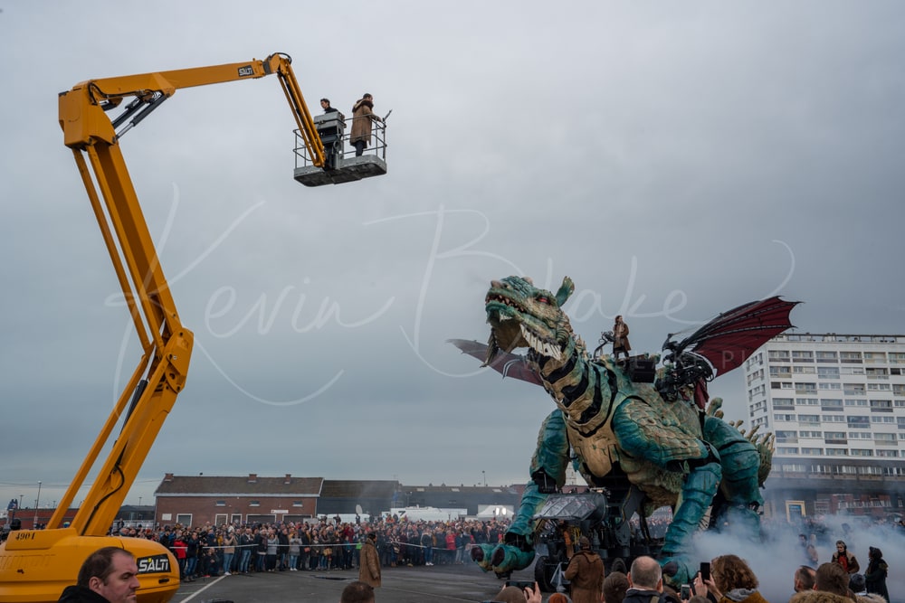Le Dragon de Calais with its wings spread beside a cherry picker carrying performers, Calais, France