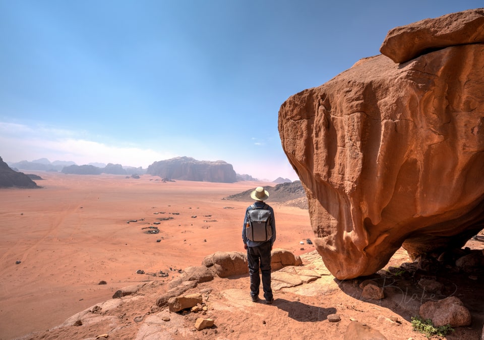 Hiker standing beside a huge sandstone boulder looking out over the red desert of Wadi Rum, Jordan
