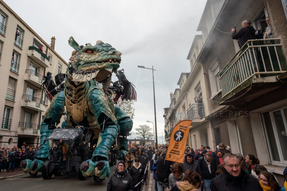 Le Dragon de Calais walking down a residential street as people watch from balconies, Calais, France