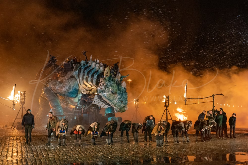 Performers bowing in front of Le Dragon de Calais at night, with flames and smoke, Calais, France