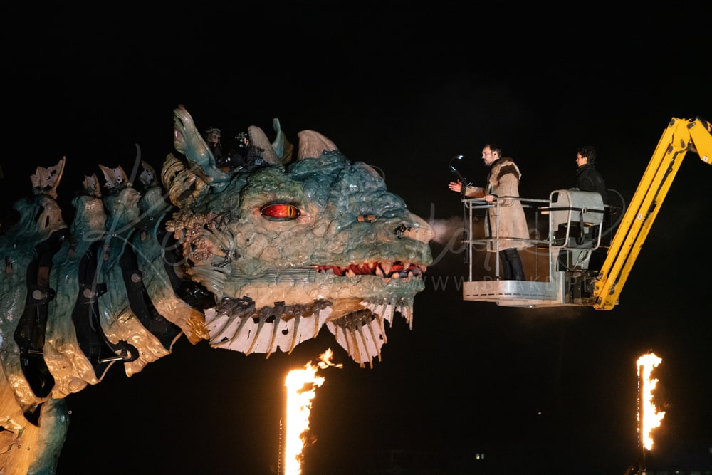 Le Dragon de Calais at night beside performers on a raised platform, with flames below, Calais, France